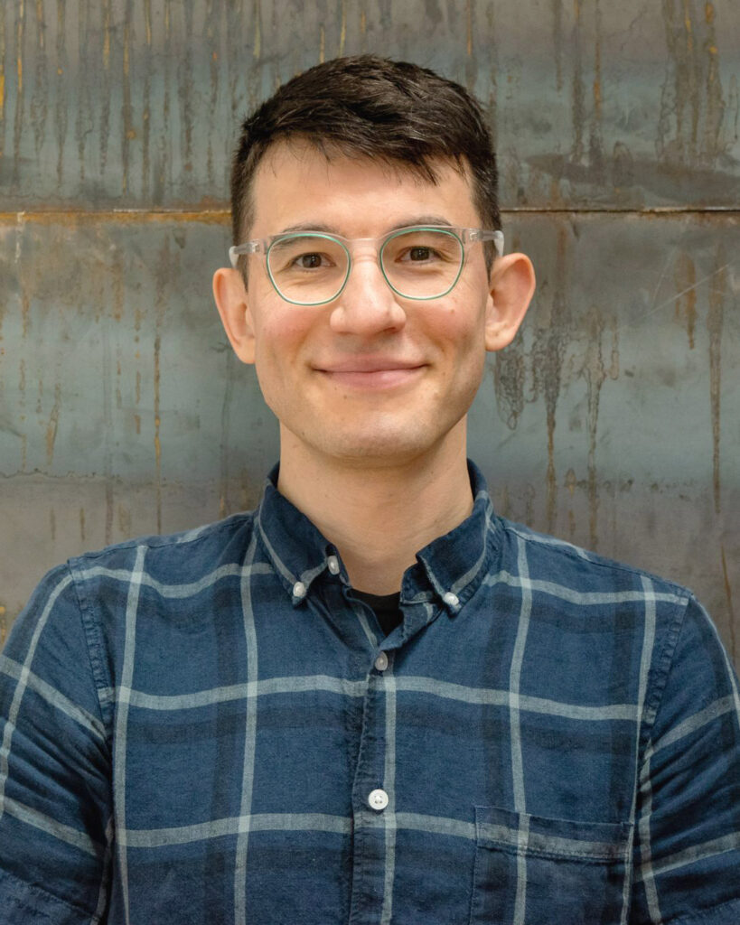 headshot of basil wearing a plaid shirt and clear glasses
